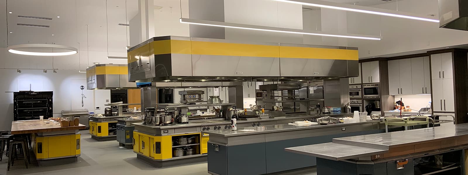 A stainless steel commercial kitchen hot line with a six-burner gas range under an extraction canopy.